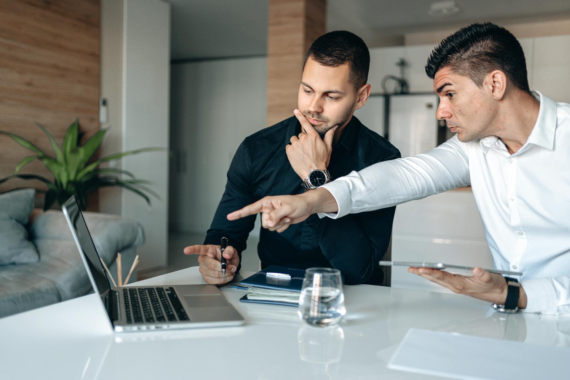 businessmen sitting next to each other while seriously looking at the screen of a laptop